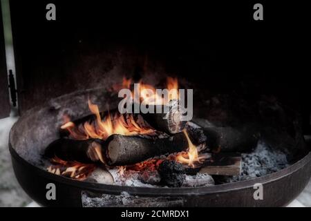 Lagerfeuer in Metallbehälter, Feuerring Nahaufnahme von brennenden Baumstämmen und hellen Flammen des Feuers Stockfoto