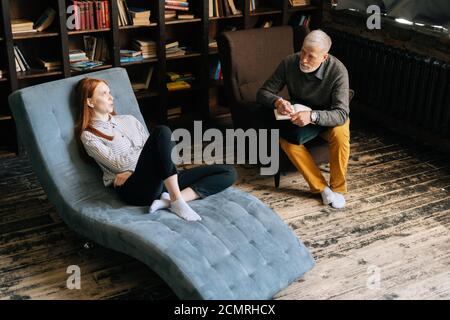 Attraktive junge Frau auf Sessel reden über seine Probleme mit reifen Mann Psychotherapeut Stockfoto