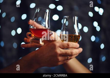 Ein Paar macht einen Toast mit zwei Gläsern Whiskey Auf festlichem Hintergrund Stockfoto
