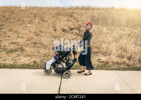 Mutter läuft ihre Jungen durch den Park in Chicago während Quarantäne trägt Gesichtsmasken Stockfoto