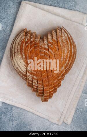 Geschnittenes rundes Roggenbrot in Herzform auf einer grauen Leinenserviette. Schmackhaftes und nützliches Backprodukt aus der Nähe. Selektiver Fokus Stockfoto