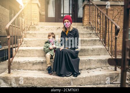 Mutter und Sohn sitzen auf der vorderen Treppe mit Gesicht Masken während der Quarantäne aktiviert Stockfoto