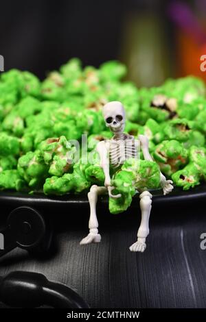 Ein Skelett sitzt am Rand eines Kessels und hält in seinen Händen ein grünes süßes Popcorn. Nahaufnahme. Ha Stockfoto