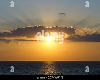 Strahlen der untergehenden Sonne bricht durch die Wolken über dem Meer Stockfoto