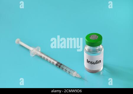 Medizinisches Fläschchen mit Insulin und einer Einmalspritze auf türkisfarbenem Hintergrund, selektiver Fokus. Gesundheitskonzept. Stockfoto