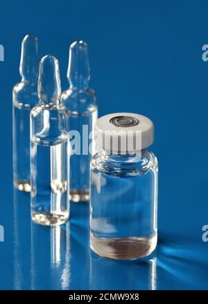 Fläschchen mit Medizin und einer Glasampulle auf blauem Hintergrund. Geringe Schärfentiefe, selektiver Fokus. Gesundheitskonzept. Stockfoto