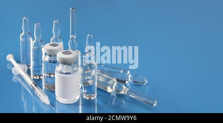 Fläschchen mit Medizin, Glasampullen und einer Einwegspritze auf hellblauem Hintergrund mit Kopierraum. Geringe Schärfentiefe, selektiver Fokus. Stockfoto
