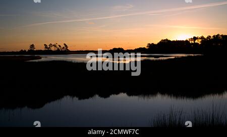 Sonnenuntergang über Assateague Island über Sümpfen, Salzwasserbucht mit der Silhouette der Insel mit Bäumen. Stockfoto