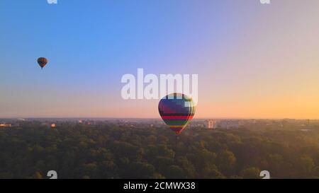 Luftdrohne Ansicht der bunten Heißluftballon fliegen über grünen Park in kleinen europäischen Stadt bei Sommersonnenaufgang, Kiew Region, Ukraine Stockfoto