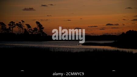 Sonnenuntergang über Assateague Island über Sümpfen, Salzwasserbucht mit der Silhouette der Insel mit Bäumen. Stockfoto