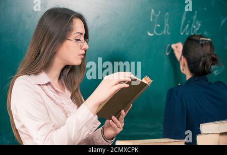 Junge lächelnde Lehrerin im Klassenzimmer Armaturenbrett mit Kreide Stockfoto