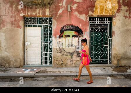 Junge Frau geht vor einem Che Guevara-Porträt Gestrichen in einem schäbigen Gebäude in der Altstadt von Havanna Stockfoto