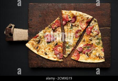 Gebackene Pizza mit geräucherten Würsten, Pilzen, Tomaten, Käse und Dill, in Scheiben geschnittenes Essen Stockfoto