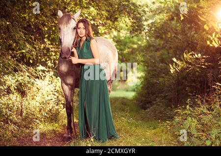 Junge elegante Frau in stilvollem Kleid und weißes Pferd Porträt Am Waldweg Stockfoto