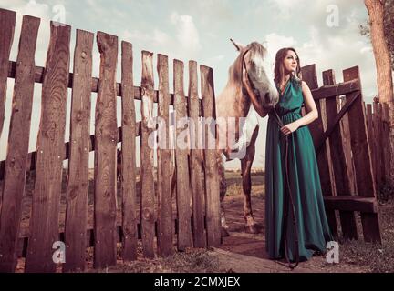 Frau in eleganten grünen Kleid und weißes Pferd auf dem Land Farmaland Holzzaun Stockfoto