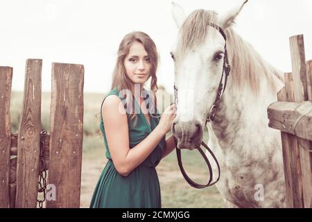 Frau in eleganten grünen Kleid und weißes Pferd auf dem Land Farmaland Holzzaun Stockfoto