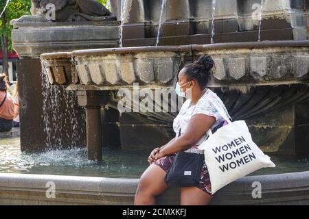 Clermont Ferrand - 08/24/2020 : Schwarze Frau mit Maske sitzt auf einem Brunnen Stockfoto