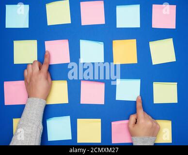 Zwei weibliche Hände und viel leeres Papier bunt Quadratische Aufkleber auf blauem Hintergrund Stockfoto