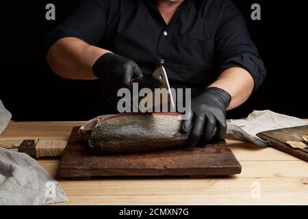 Chef in schwarzem Hemd und schwarzen Latexhandschuhen Scheiben ein Ganz frischer Fischlachs Stockfoto