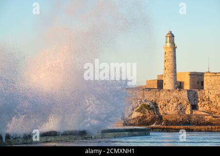 El morro Festung und Leuchtturm von Havanna bei Sonnenuntergang mit Riesige Meereswellen, die auf dem Malecon Damm krachen Stockfoto