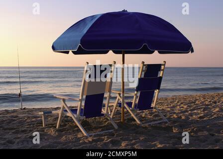 Liegestühle unter einem Sonnenschirm am Strand bei Sonnenaufgang. Stockfoto