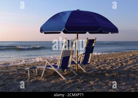 Liegestühle unter einem Sonnenschirm am Strand bei Sonnenaufgang. Stockfoto