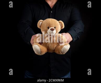 Ein erwachsener Mann in einem schwarzen Hemd hält einen braunen Teddy Bär Stockfoto