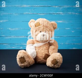 Brauner Teddybär mit aufgewickelter weißer Bindungpfote auf einer Blauer Holzhintergrund Stockfoto
