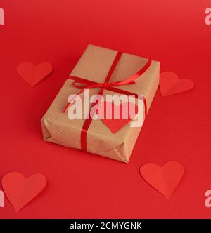 Box in braunem Kraftpapier verpackt und mit einem roten dünnen Seidenband gebunden, aus Papierherzen geschnitten, rot Stockfoto