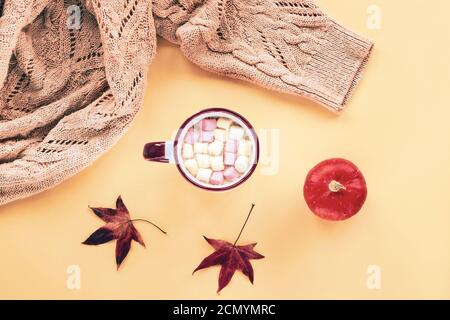 Eine Tasse Kakao mit Marshmallows, Strickpullover, Kürbis und Herbstblätter auf gelbem Hintergrund, Herbstkonzept. Draufsicht, flach liegend. Stockfoto