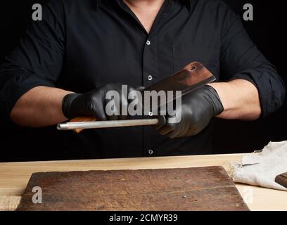 Koch in einem schwarzen Hemd und schwarzen Latexhandschuhen schärfen Ein Küchenmesser Stockfoto