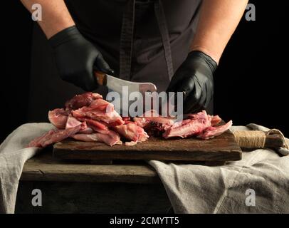 Koch in schwarzen Latexhandschuhen hält ein großes Messer und Schneidet rohes Kaninchenfleisch in Stücke Stockfoto