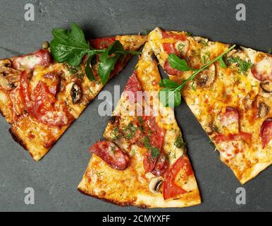 Gebackene runde Pizza mit geräucherten Würsten, Pilzen, Tomaten, Käse und Rucola-Blättern Stockfoto