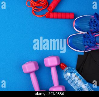 Kunststoff lila Hanteln, Sportbekleidung, Wasser, rosa Sneakers auf blauem Hintergrund Stockfoto
