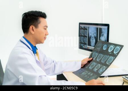 Asiatischer Mann Arzt hält und schaut zu untersuchen Röntgenbild des Patienten Schädel und Gehirn in einer medizinischen Klinik im Krankenhaus. Stockfoto