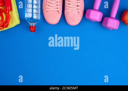 Kunststoff lila Hanteln, Sportbekleidung, Wasser, rosa Sneakers auf blauem Hintergrund Stockfoto