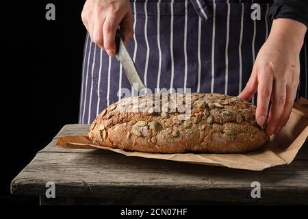 Frau in einer blauen Schürze mit einem Messer in ihr Hand über rund gebackenes Brot zu schneiden Stockfoto