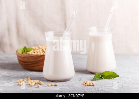 Bio-Sojamilch ohne Milchprodukte in Glas und Holzplatte mit Sojabohnen auf grauem Betongrund. Vegan gesundes Lebensmittelkonzept, Nahaufnahme, Seitenansicht. Stockfoto