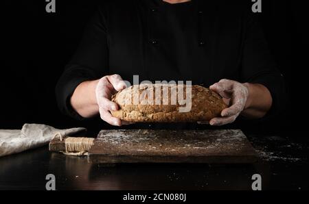 Männliche Hände halten braungebackenes Roggenbrot über Holz Brett mit Mehl Stockfoto
