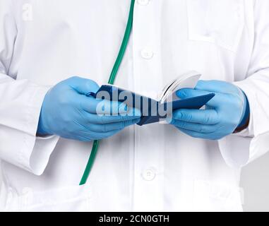 Arzt in einem weißen Mantel und blauen Handschuhen hält ein Notizbuch aus blauem Papier für Notizen Stockfoto