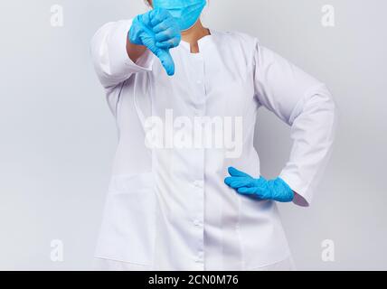 eine medizinerin in einem weißen Mantel und einer Maske, die blaue medizinische Latexhandschuhe an den Händen trägt, zeigt eine Dislik Stockfoto