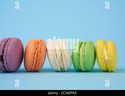Mehrfarbige runde gebackene Macarons Kuchen auf hellblauem Hintergrund, Dessert steht in einer Reihe Stockfoto