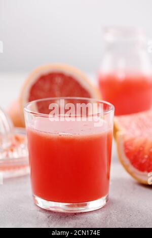 Ein Glas frisch zubereiteter Grapefruitsaft und Scheiben frischer Früchte auf hellem Betonboden. H Stockfoto