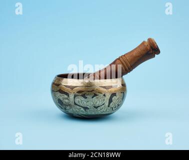 Kupferne Klangschale und Holzstab auf blauem Hintergrund, ein tibetisches Musikinstrument Stockfoto