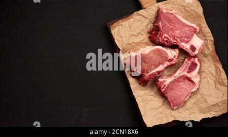 Drei rohe, saftige Schweinefleischscheiben auf der Rippe, Lebensmittel liegen auf braunem Pergamentpapier Stockfoto