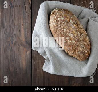 Gebackenes ovales Brot aus Roggenmehl mit Kürbiskernen Auf einer grauen Leinenserviette Stockfoto