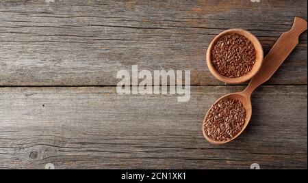 Trocknen Sie braune Leinsamen in einem braunen Holzlöffel auf Ein grauer Holztisch aus alten Brettern Stockfoto