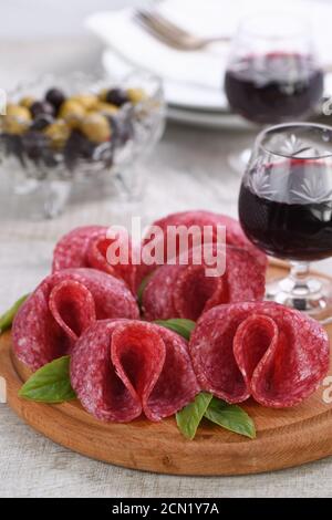 Leichte Mahlzeit Snack aus Salami gefaltet in Form einer Blume mit einem Glas Sherry auf einer Holzschale. Cl Stockfoto