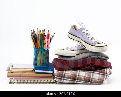 Stapel gefalteter Kleidung, Sport-Sneakers, Papeterie auf weißem Hintergrund Stockfoto