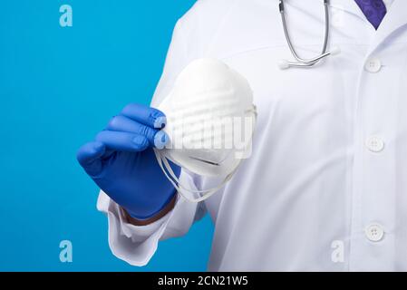 Männlicher Arzt in blauem Latex sterile Handschuhe hält eine weiße Einwegmaske aus Vlies Stockfoto